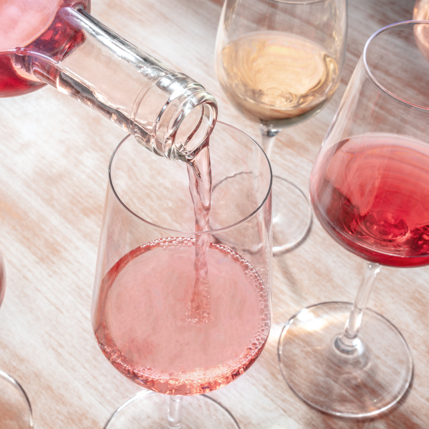 pouring nonalcoholic rose wine into a glass. glass of nonalcoholic red and white wine on the side