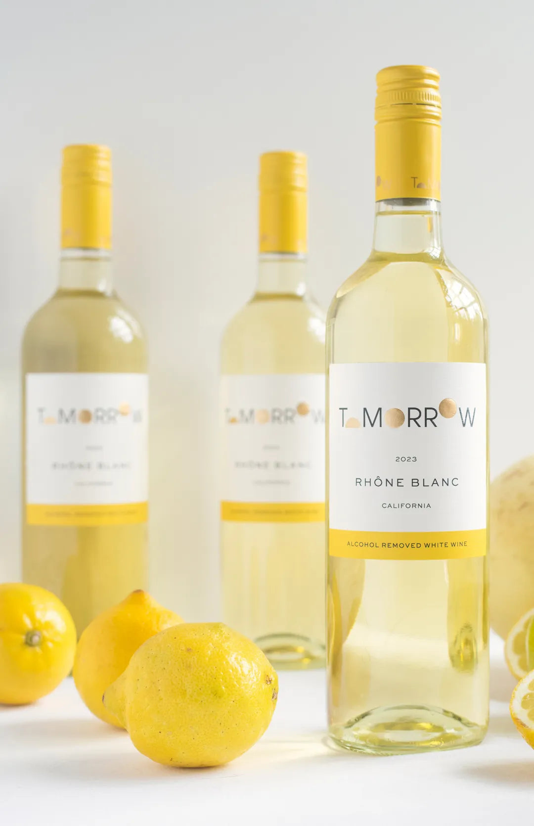 Three bottles of Nonalcoholic Tomorrow Rhone Blanc and several lemons against a white backround