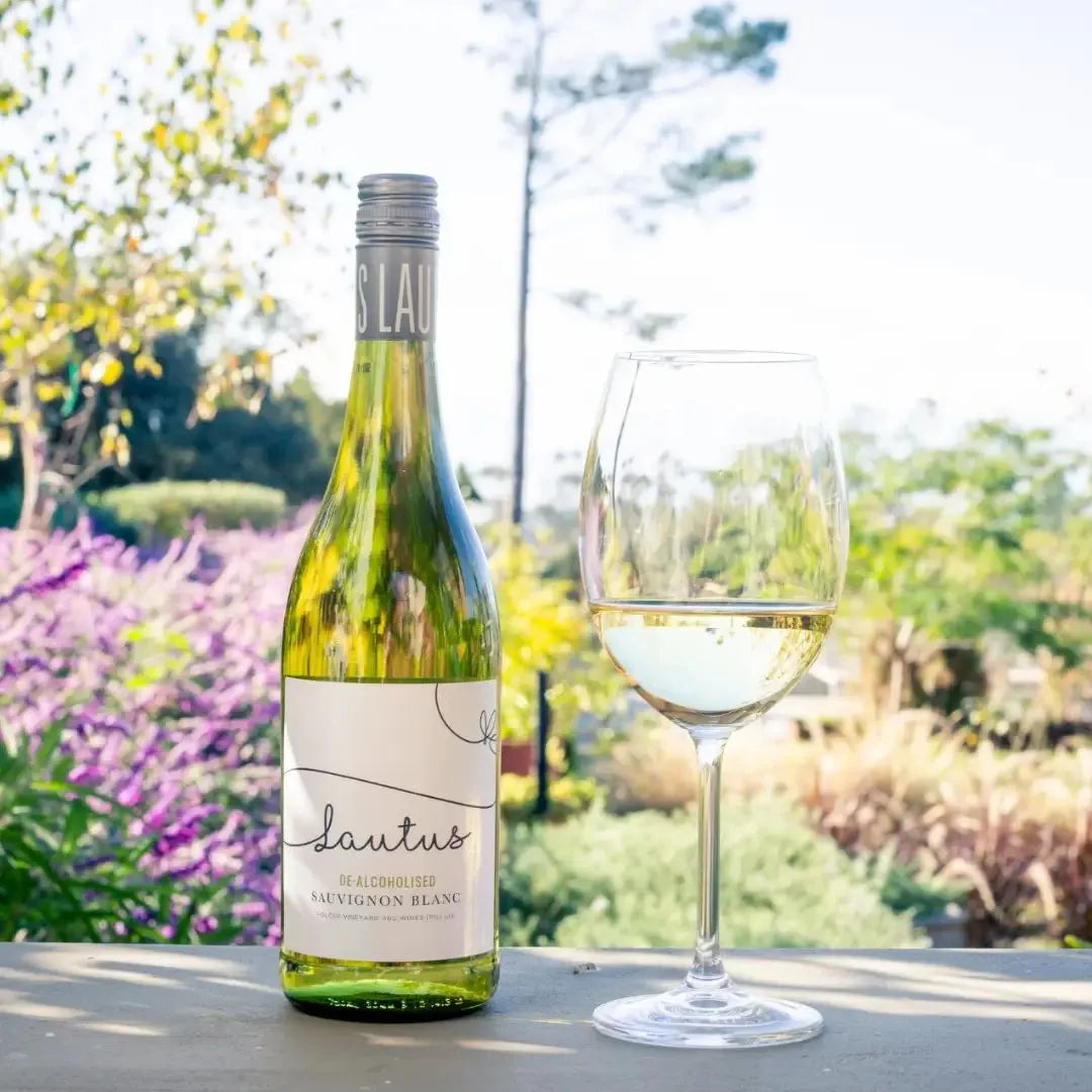 Bottle of Lautus De-alcoholized Sauvignon Blanc on a table next to a wine glass in a garden setting
